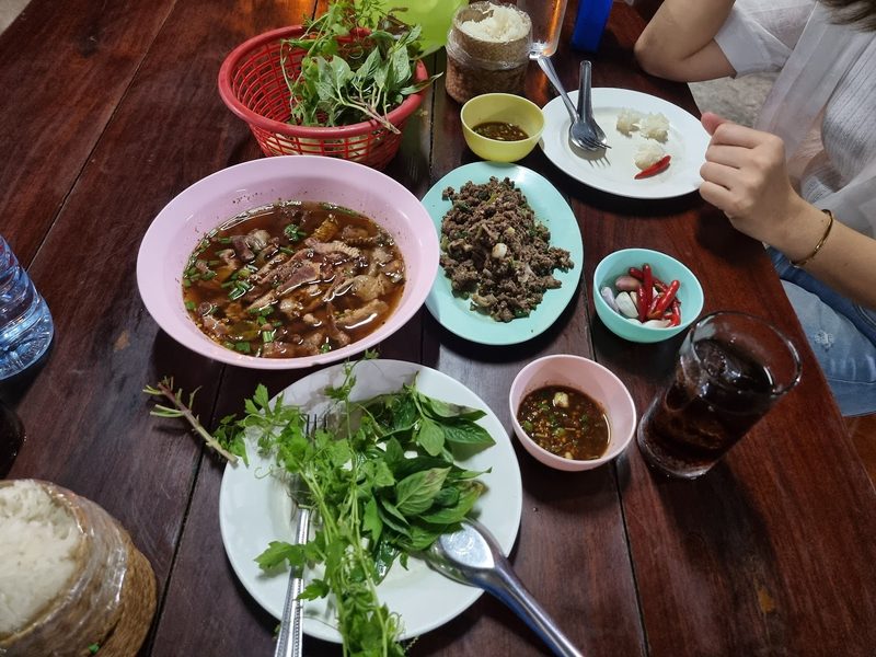 สำรับบนโต๊ะไม้ มีต้ม ลาบ ผักสด และกระติบข้าวเหนียว