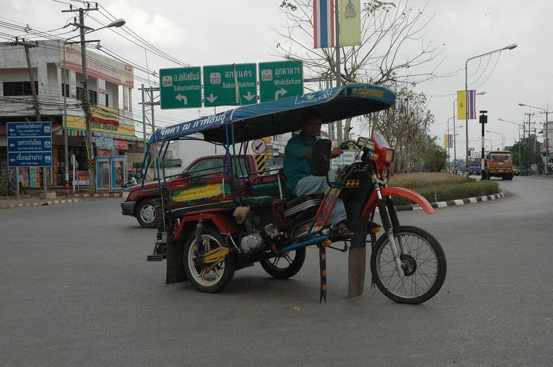 สามล้อเครื่องหลังคาผ้าใบจอดที่หัวมุมถนน ด้านหลังมีป้ายบอกทาง